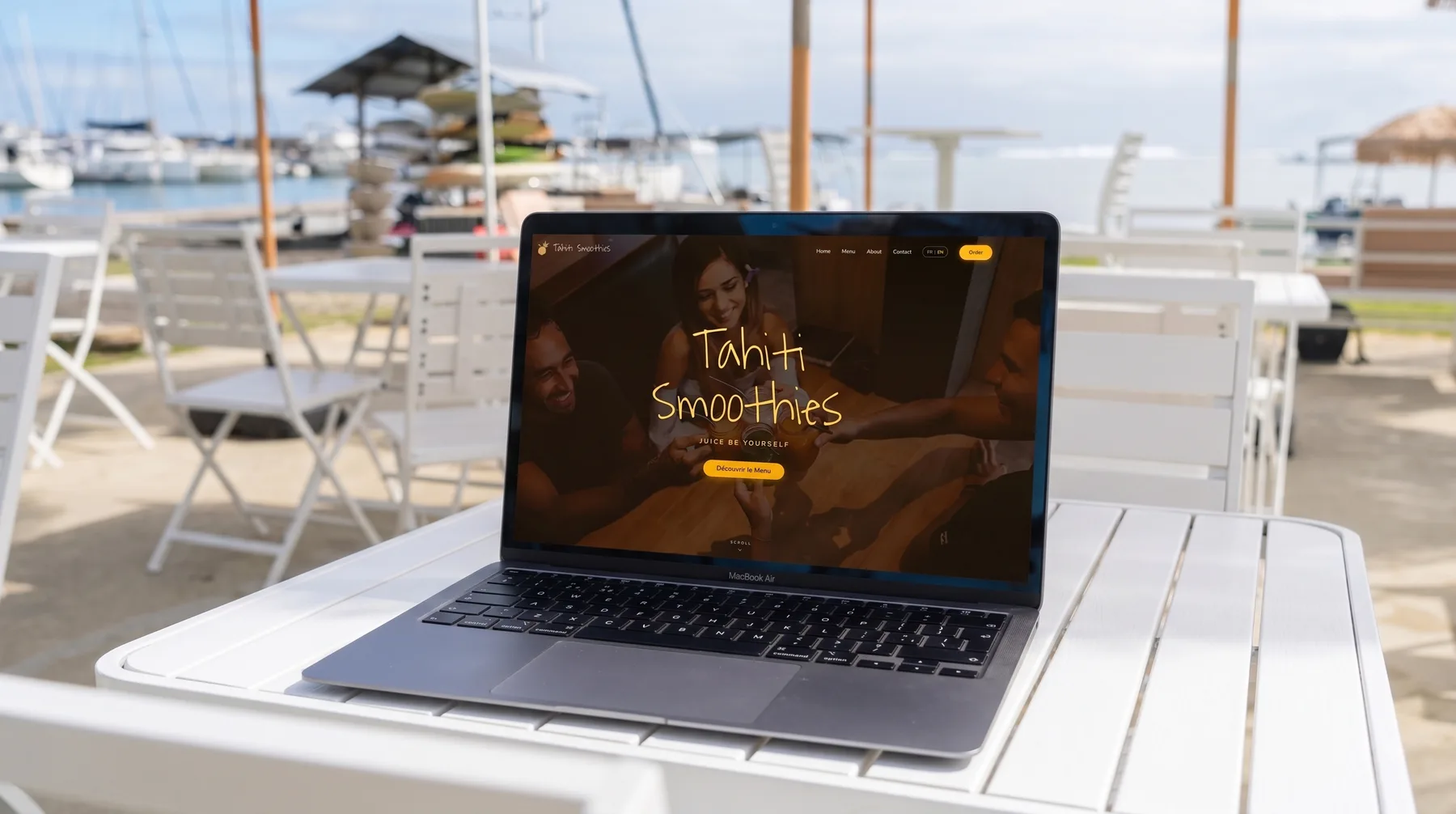 Le site Tahiti Smoothies ouvert sur un ordinateur portable, posé sur une table blanche face aux bateaux de la marina.